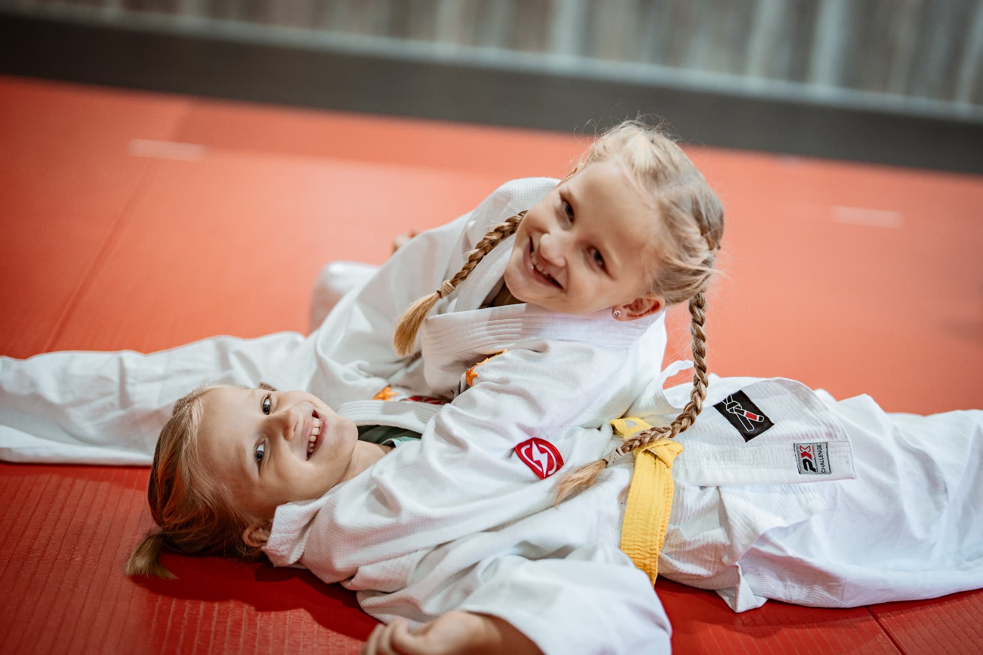 Zwei Kinder im Trainingsanzug lachen auf der roten Matte im SAO-DOJO Geldern