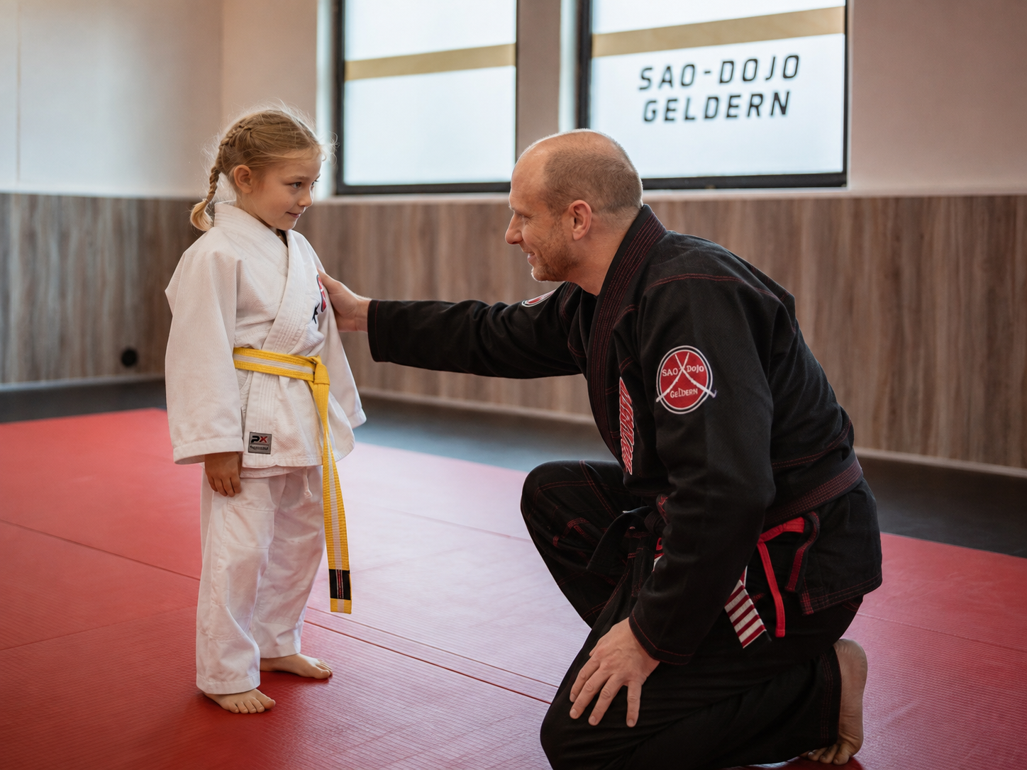 Trainer kniet auf Augenhöhe vor einem Kind im weißen Anzug im SAO-DOJO Geldern