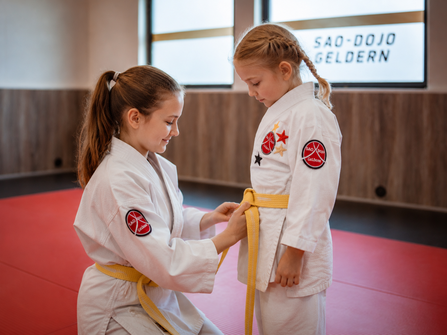 Älteres Kind bindet einem jüngeren Kind den gelben Gürtel im SAO-DOJO Geldern