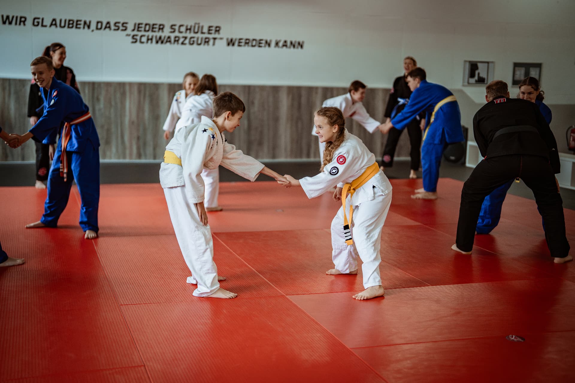 Junge und Mädchen trainieren im weißen Anzug miteinander auf der roten Matte im SAO-DOJO Geldern, weitere Kinder im Hintergrund